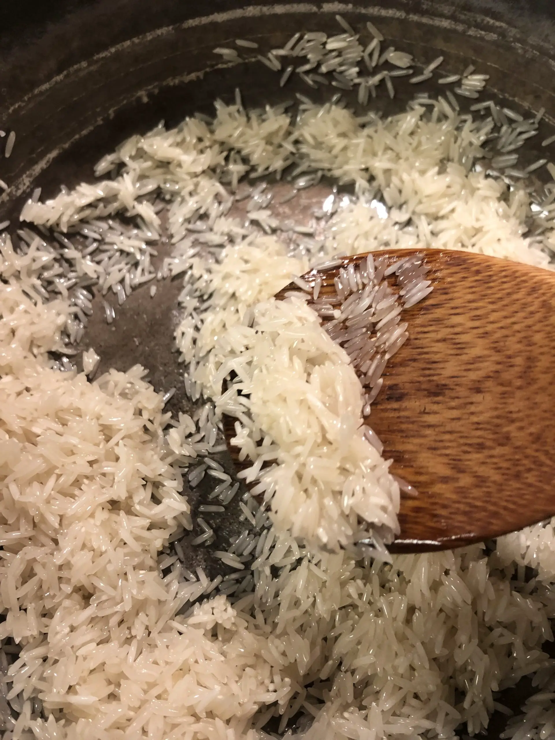Grains of rice coated in oil with a wooden spoon