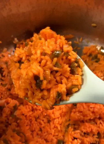Spicy Mexican Rice in a pot with a blue spoon holding some of the rice.