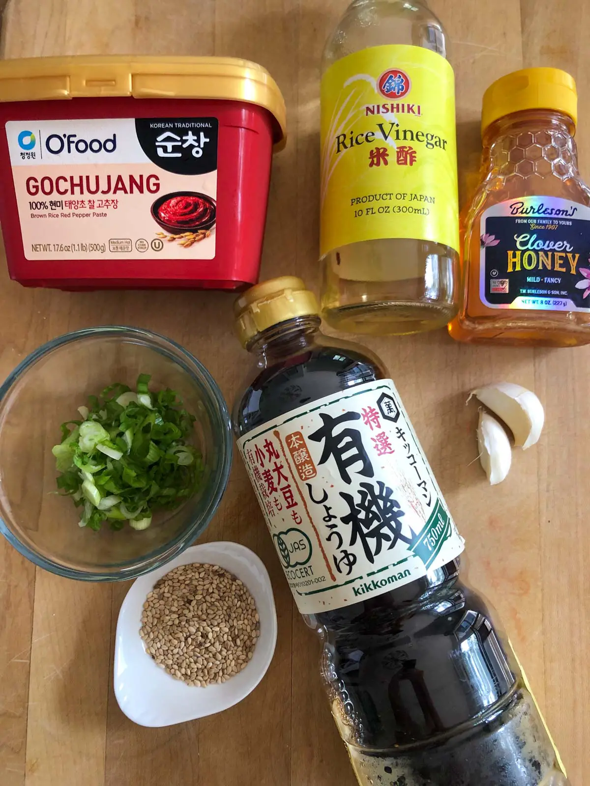 Gochujang, rice vinegar, honey, sliced green onions in a glass bowl, sesame seeds, soy sauce, and 2 cloves of garlic.