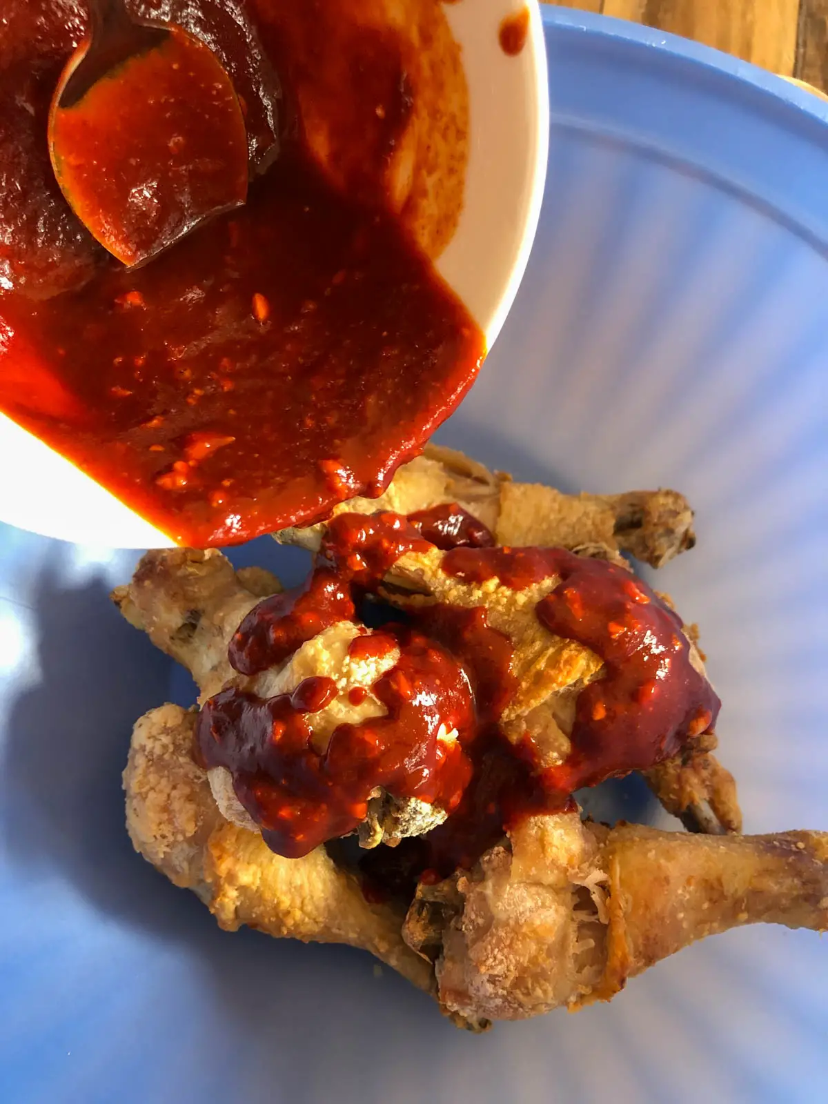 Baked chicken drumsticks in a blue bowl with gochujang based sauce being poured over them.