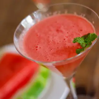 Martini glass filled with watermelon mocktail garnished with mint and a white plate with watermelon slices.