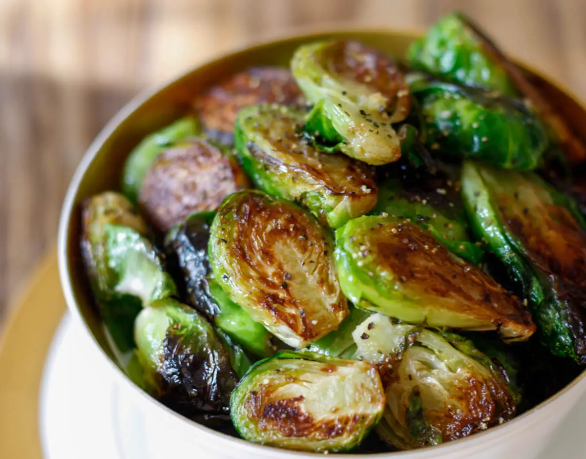 Pan fried brussels sprouts with pepper in a gold rimmed bowl.