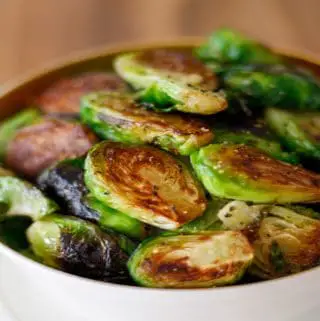 Pan fried brussels sprouts with pepper in a gold rimmed bowl.
