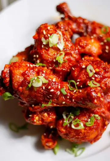 Korean Baked chicken with green onions and sesame seeds on a white plate.