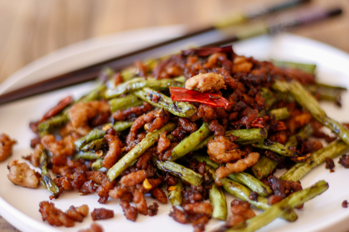Chinese Long Beans With Pork on a white plate with chopsticks in the background.