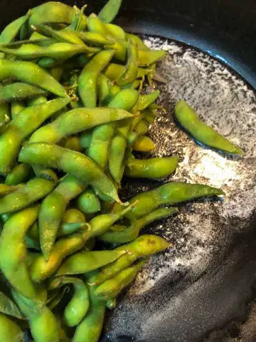 Edamame in their pods on the left side and melted butter on the right side in a cast iron pan.