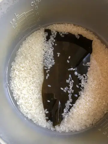 Sushi rice covered with water and a piece of kombu in the bowl of a rice cooker.