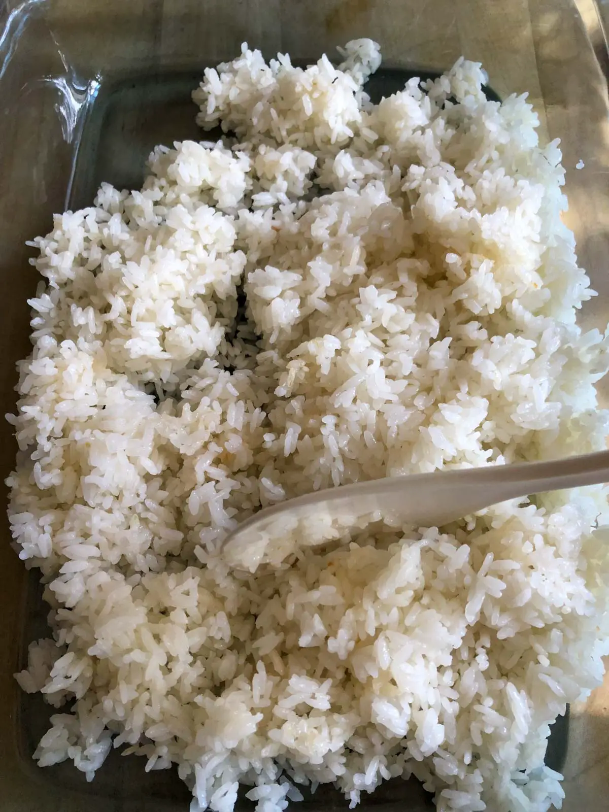 Sushi rice in a glass dish with a hand holding a rice paddle