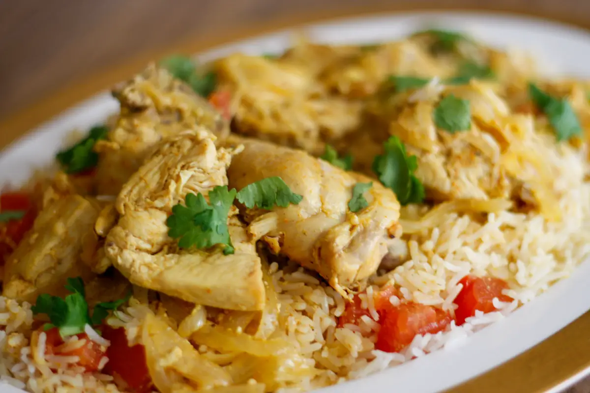 Chicken biryani with chicken pieces, rice, onions, cilantro and tomatoes on a gold rimmed plate