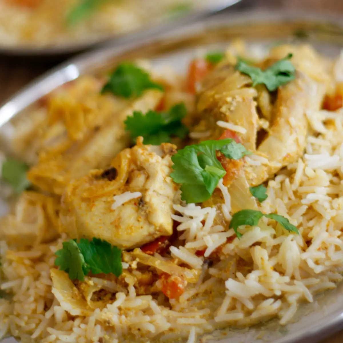 Chicken biryani with chicken pieces, rice, onions, cilantro and tomatoes on a silver plate
