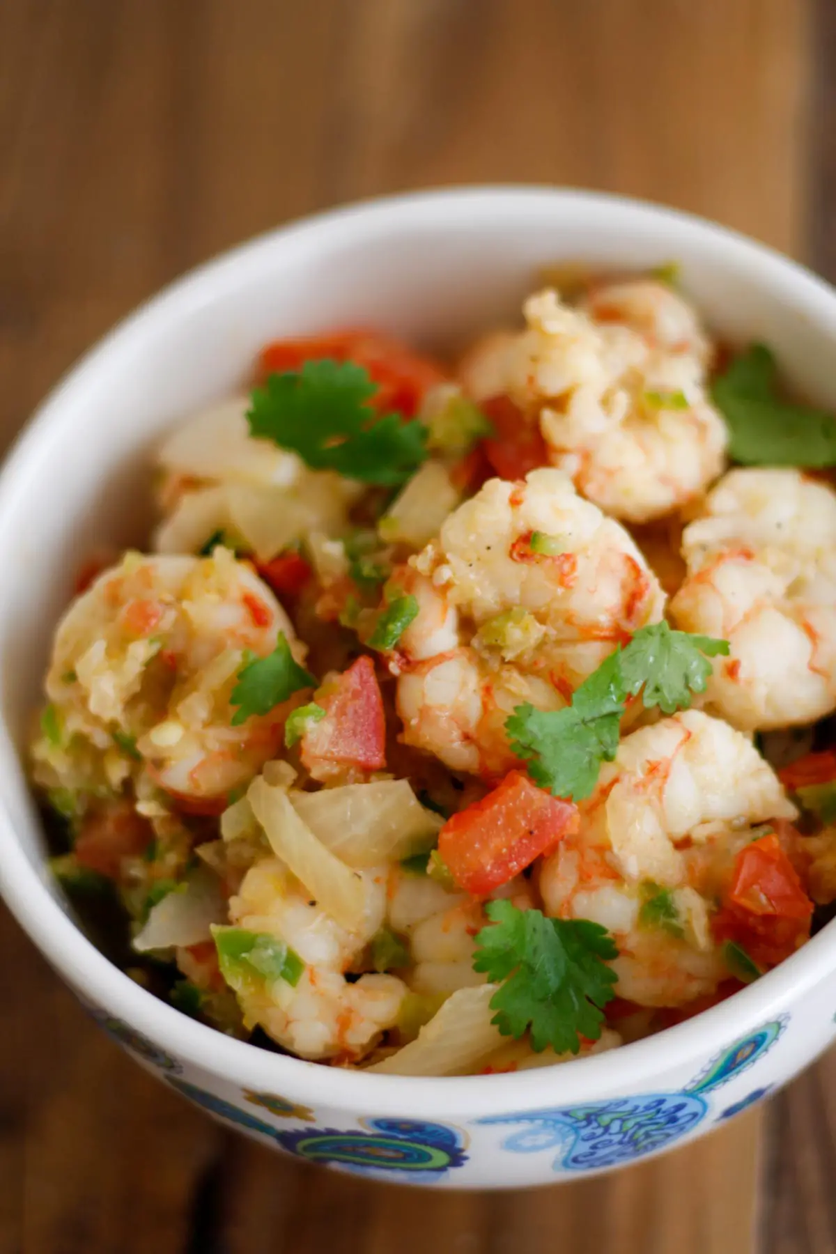 Shrimp with diced tomatoes, cilantro and onion in a white bowl with a blue paisley design