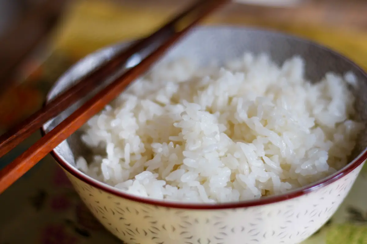 Sushi rice in a bowl with a pair of wooden chopsticks on the left hand side