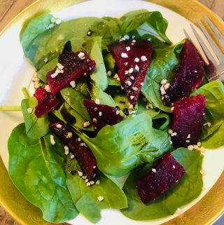 Roasted Beets and Spinach Salad in a gold rimmed bowl with a fork on the side.