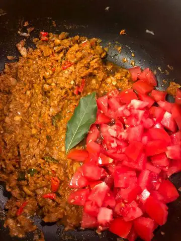 Garlic, onion, ginger and chilies in mixed spices, bay leaf and diced tomato in a pot