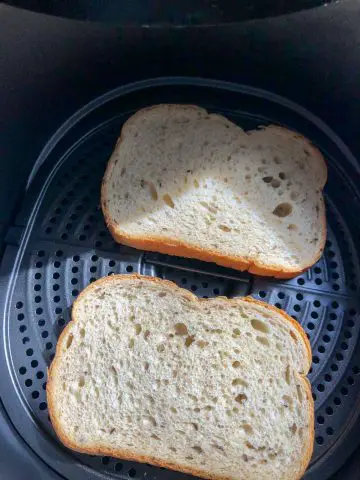 2 pieces of untoasted rye bread in an air fryer basket.