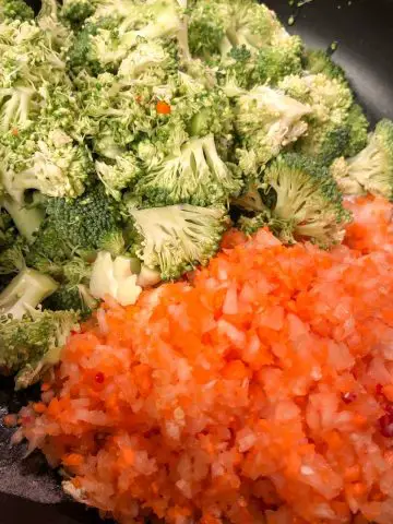 Broccoli florets and minced carrot and onion in a saucepan.