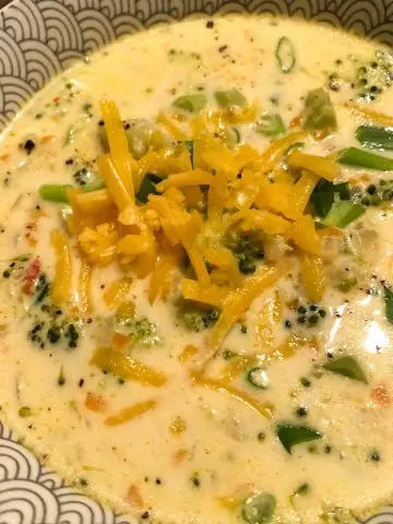 Broccoli and cheddar soup in a patterned bowl with green onions and shredded cheddar cheese as garnish.