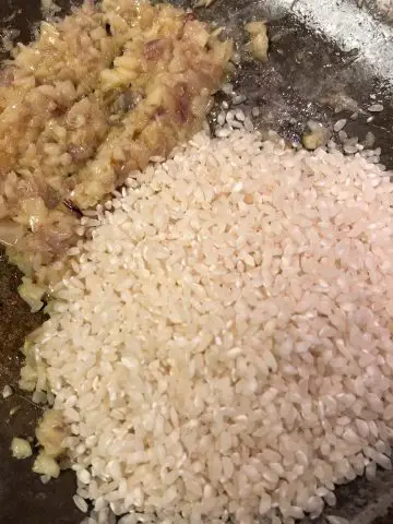 Risotto rice next to a mixture of shalllots and garlic in a skillet.