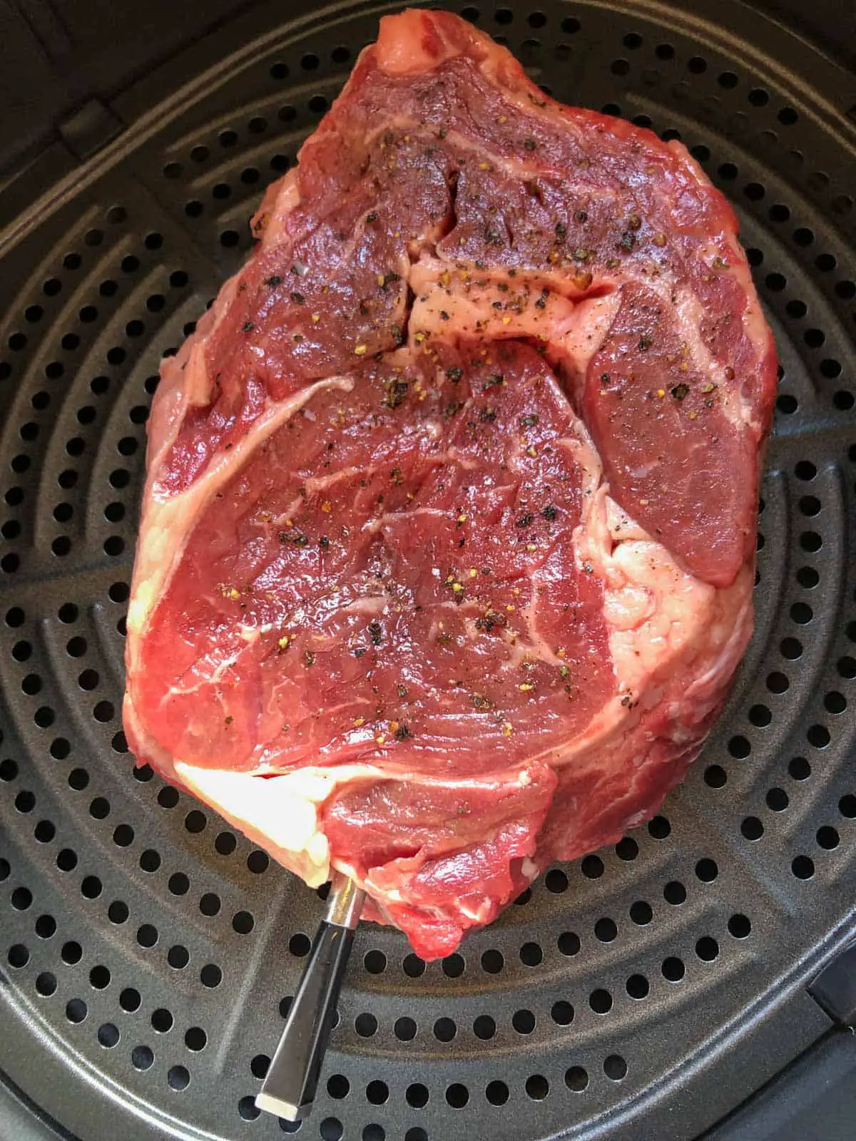 A ribeye steak with a Meater thermometer inserted in it placed in an Air Fryer basket.