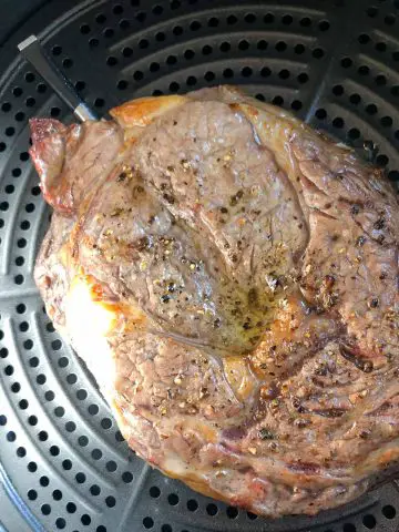 A cooked ribeye steak with a Meater thermometer inserted in it which has been placed in an air fryer basket.