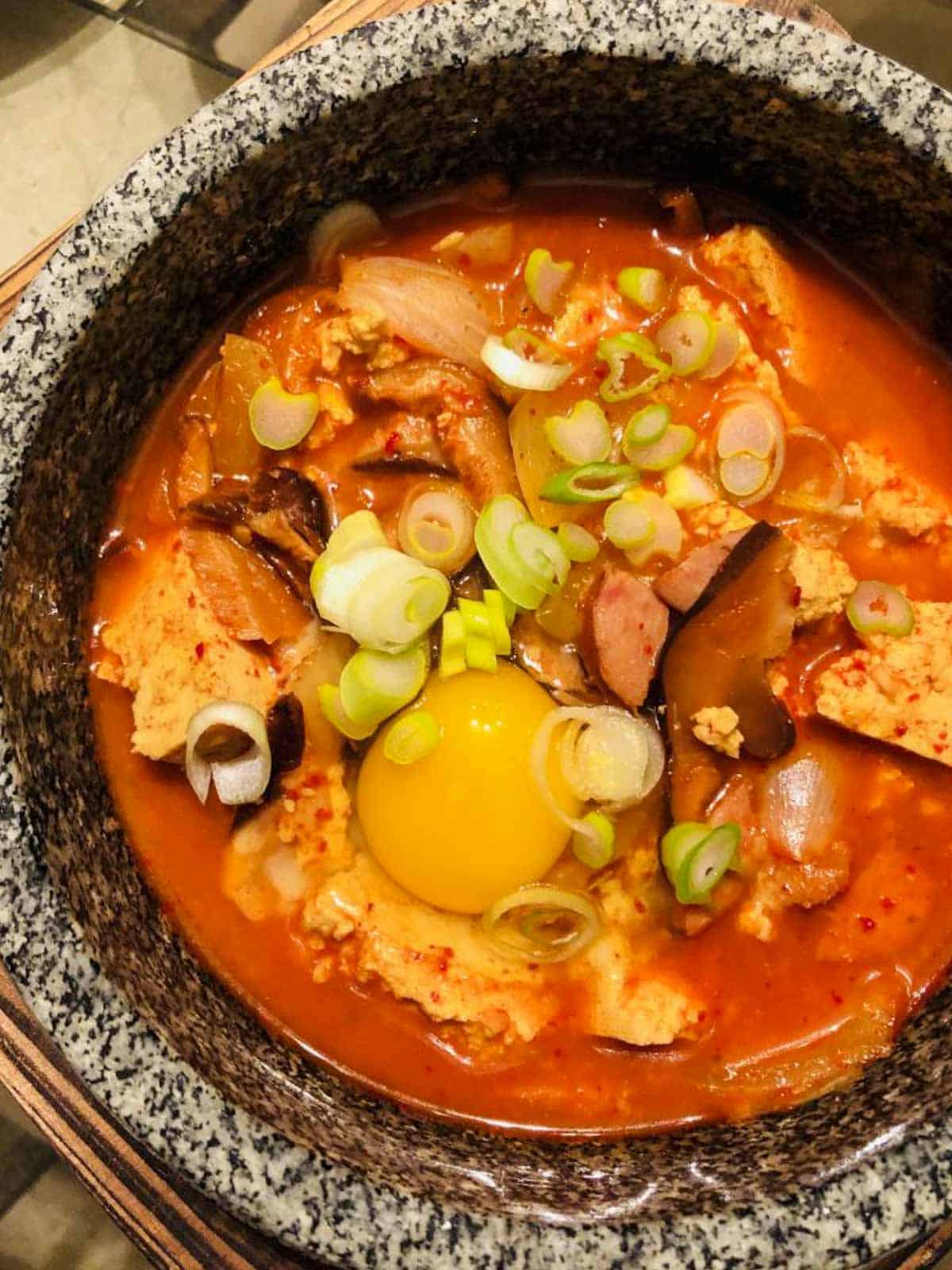 Korean Soft Tofu Stew in a clay pot with an egg yolk and green onions as garnish