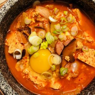 Korean Soft Tofu Stew in a clay pot with an egg yolk and green onions as garnish