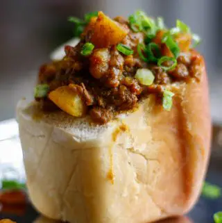 Lamb curry with potatoes inside a hollowed out piece of white bread with green onions as garnish