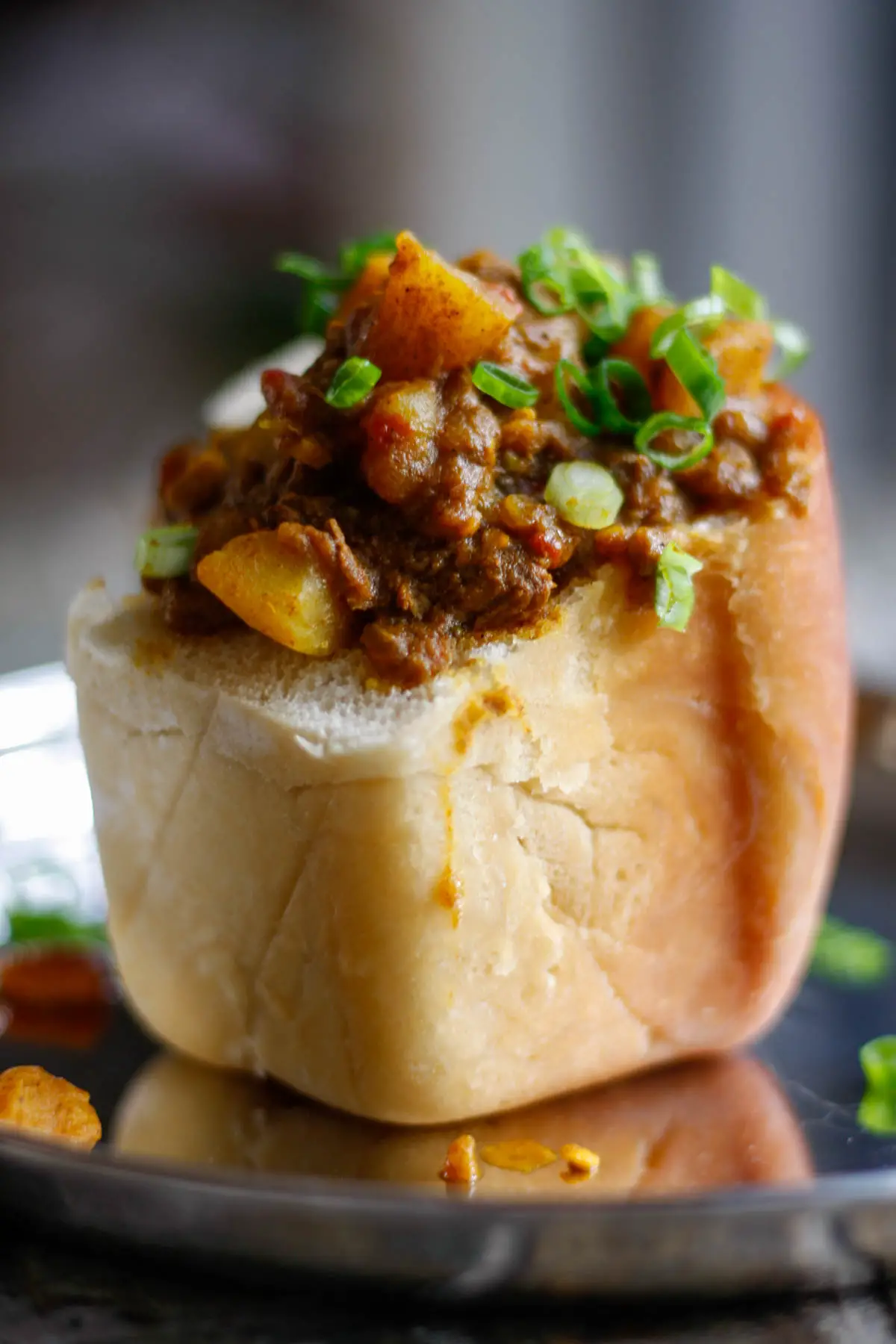 Lamb curry with potatoes inside a hollowed out piece of white bread with green onions as garnish