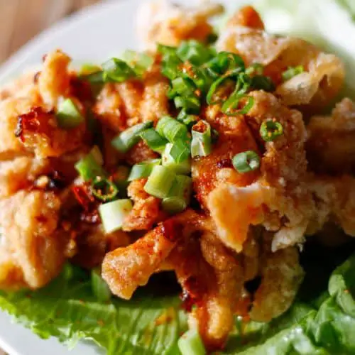 Pieces of fried chicken atop iceberg lettuce drizzled with a soy based sauce and topped with sliced green onions.