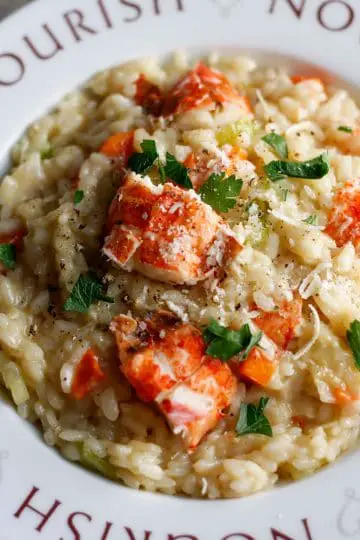 Lobster risotto garnished with parsley and Parmigiano Reggiano in a white bowl with the word Nourish on it and hearts.