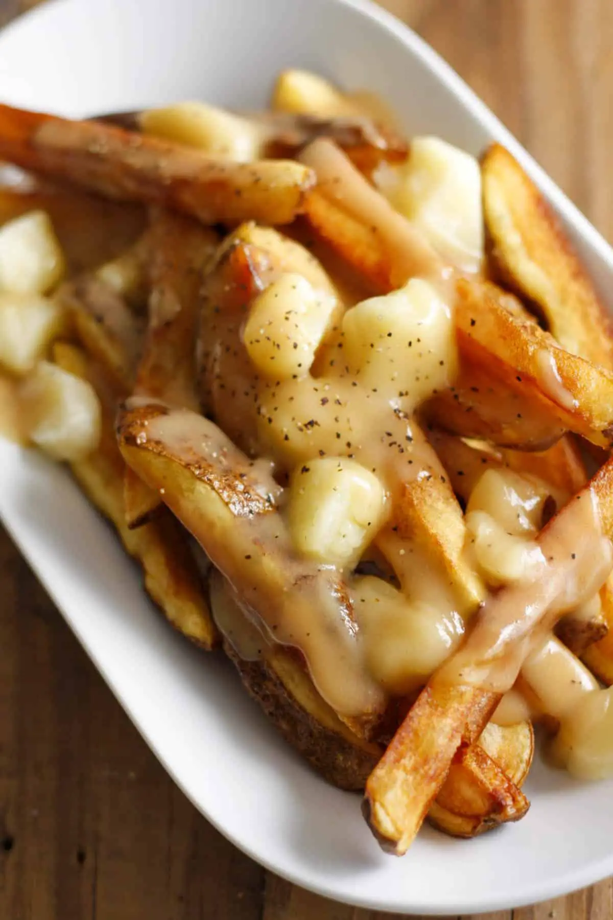Poutine consisting of fries covered with cheese curds and gravy in a white dish