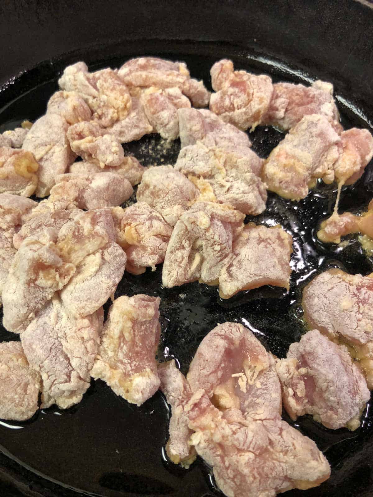 Chicken pieces that have not been cooked and are coated with egg and flour in a cast iron pan.