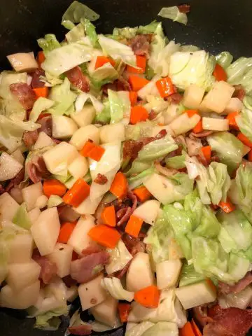 Pieces of diced bacon, cut up cabbage, potatoes and carrots in a pot.