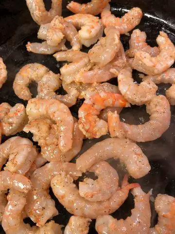 Several uncooked shrimp in a hot cast iron pan.