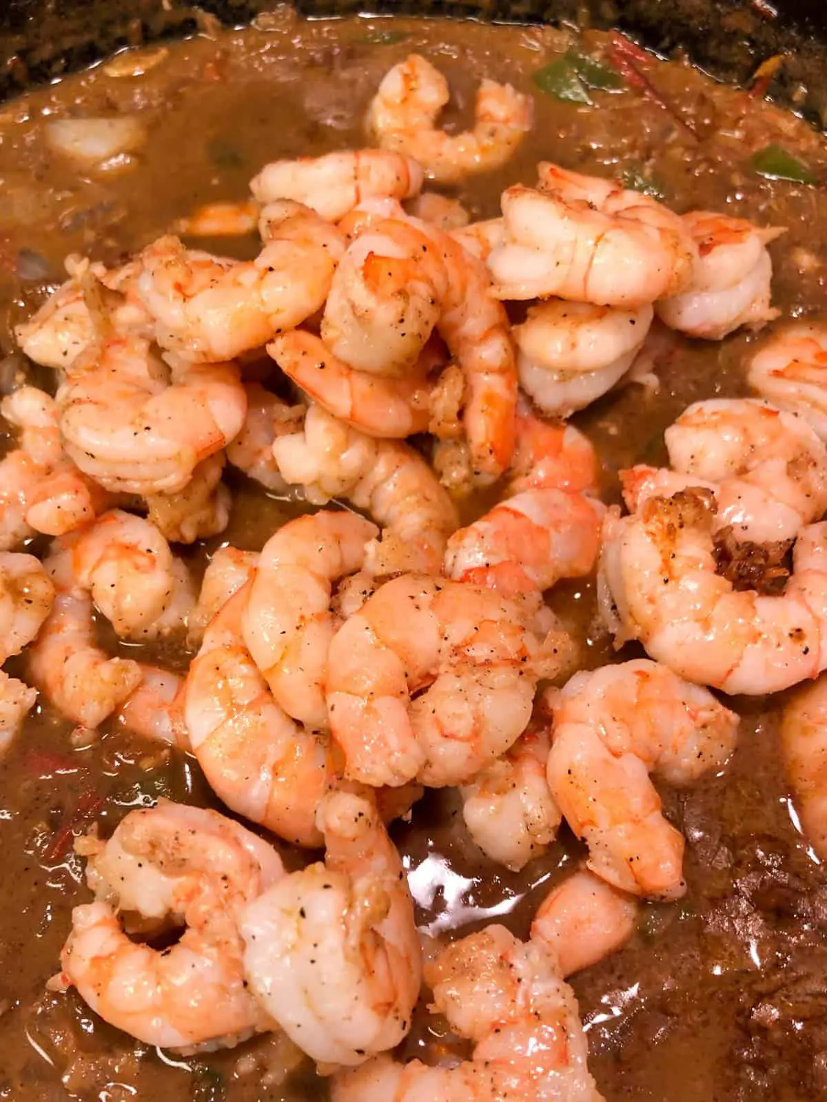 Cooked shrimp added to a dark curry sauce in a cast iron pan.