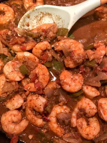 Shrimp with green bell pepper, onions, and tomatoes in a dark curry sauce with a blue silicone spoon.
