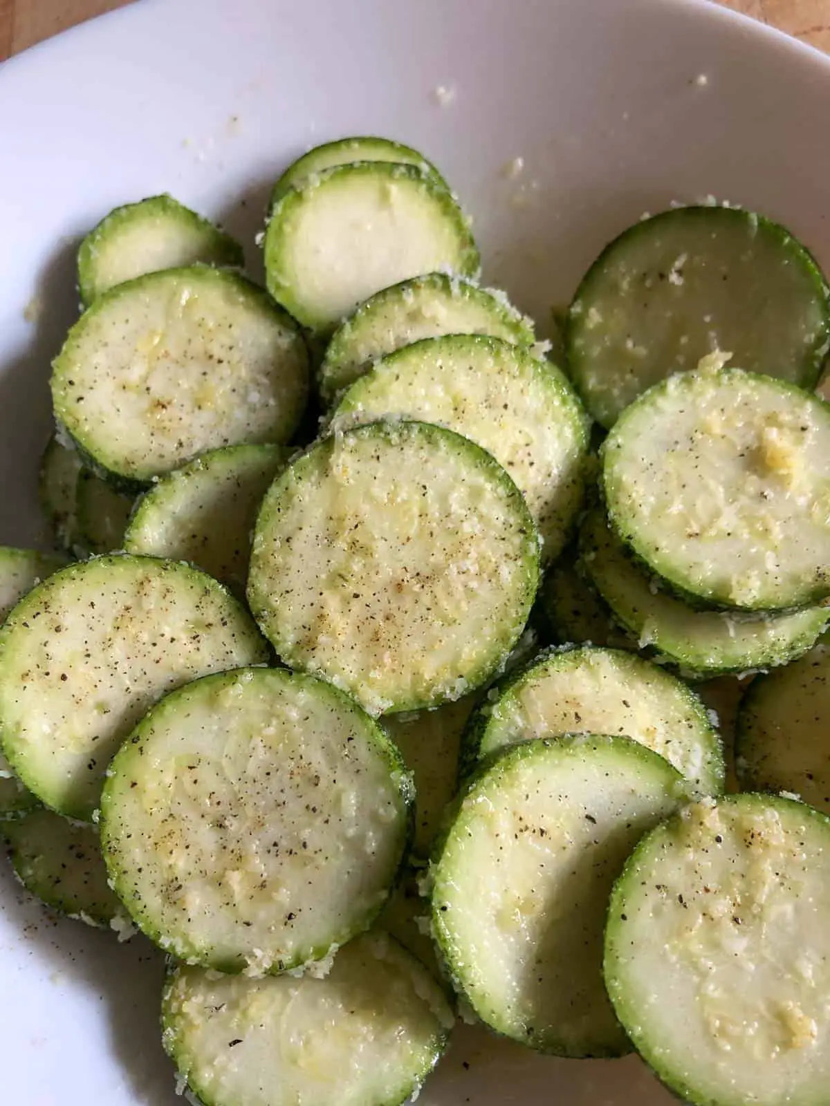 Zucchini disks coated with spices and Parmesan cheese in a white bowl.