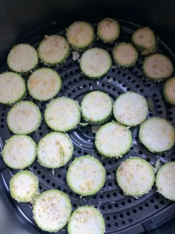 Zucchini disks coated with spices and Parmesan cheese in an air fryer basket