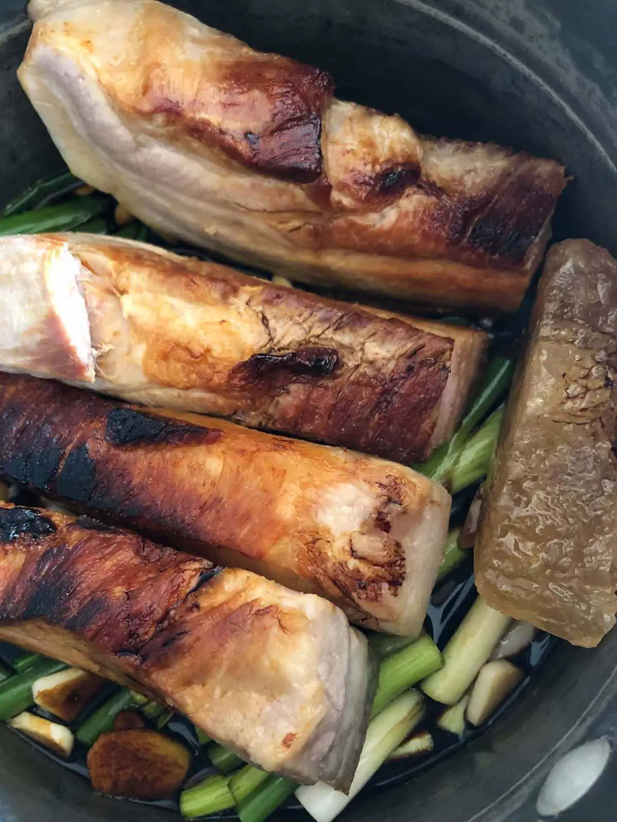 Browned slabs of pork belly and Chinese rock candy atop a soy sauce based sauce and also sitting atop slices of green onions, ginger, and garlic.