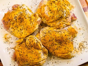 Chicken thighs with skin seasoned with salt, pepper, and turmeric on a plate.