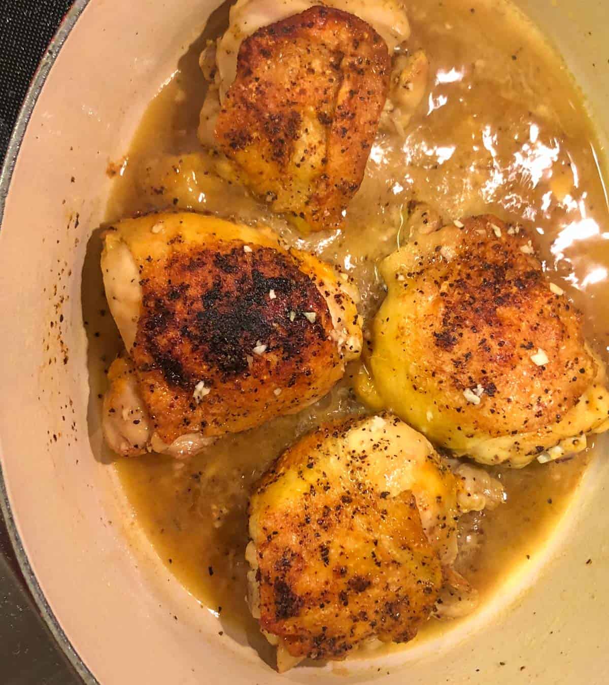 Chicken thighs which have been browned and are braising in a braising sauce in a dutch oven.