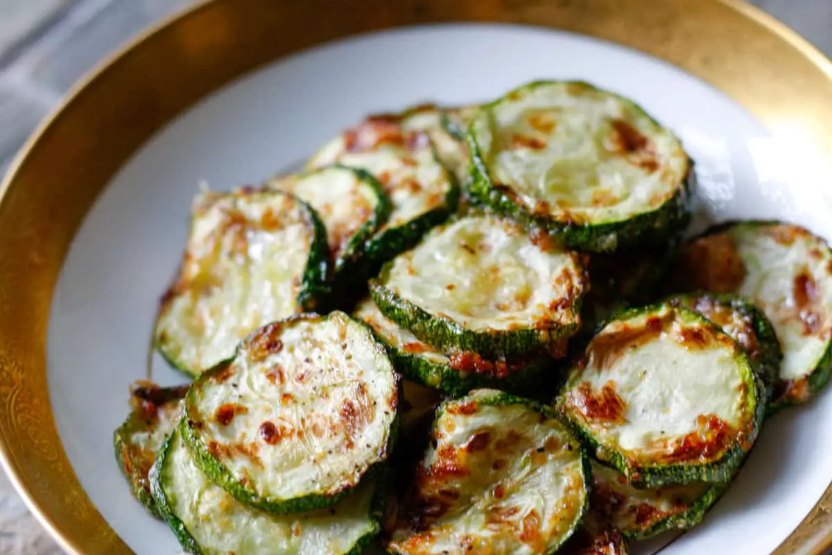 Zucchini disks which have been roasted with browned cheese on top in a gold rimmed bowl.