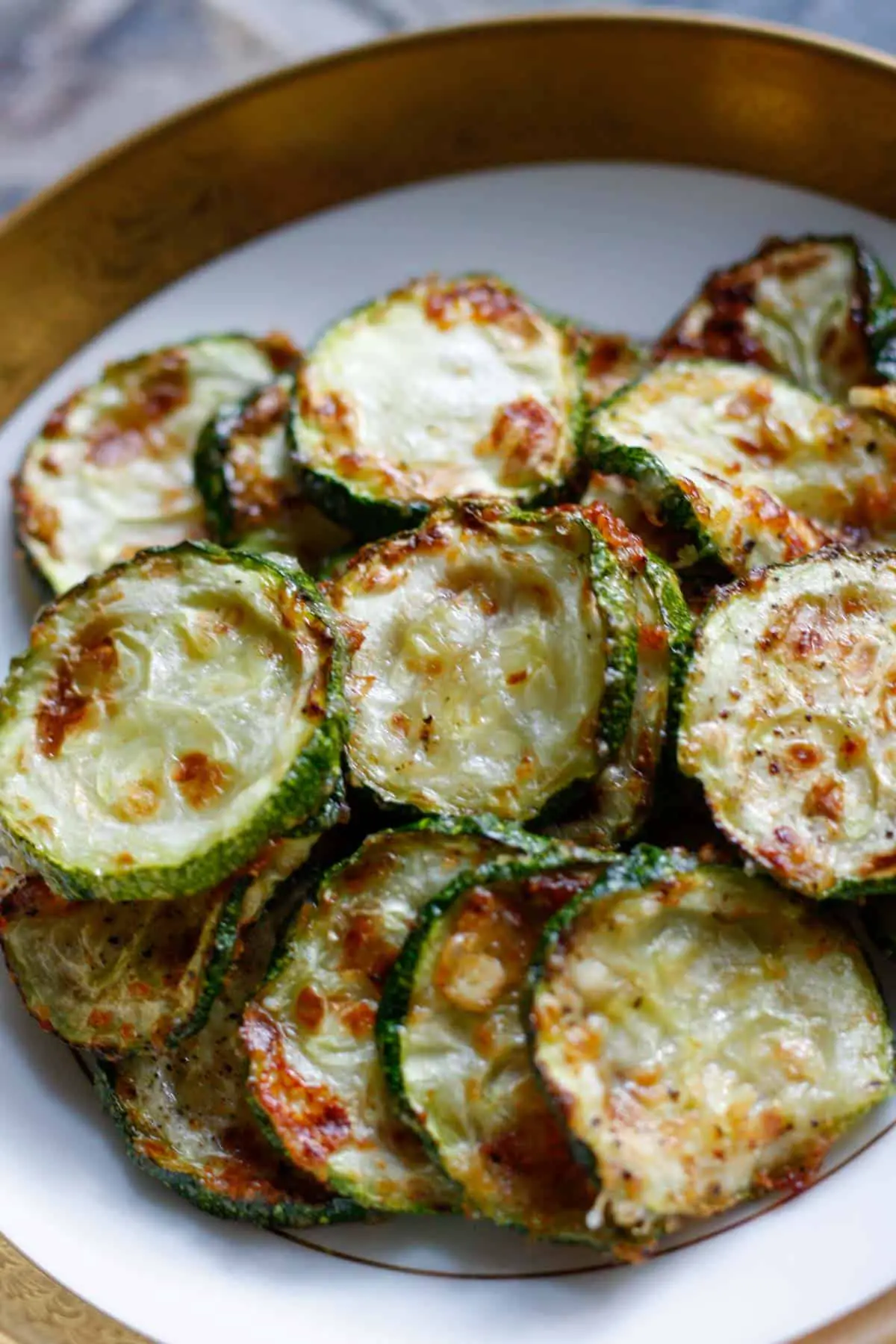 Zucchini disks which have been roasted with browned cheese on top in a gold rimmed bowl.