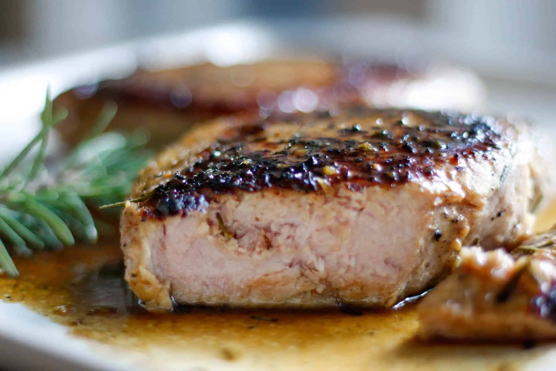 Pork chops with rosemary and caramelized sauce with one of the pork chops cut into.