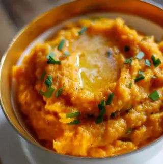 Mashed sweet potatoes in a gold rimmed bowl with melted butter and chives on top of the mashed potatoes.