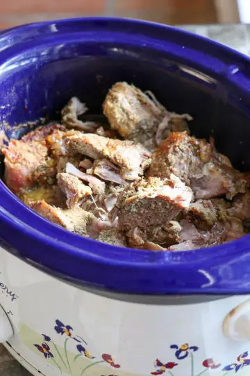 A blue crockpot filled with cook pork for carnitas tacos.