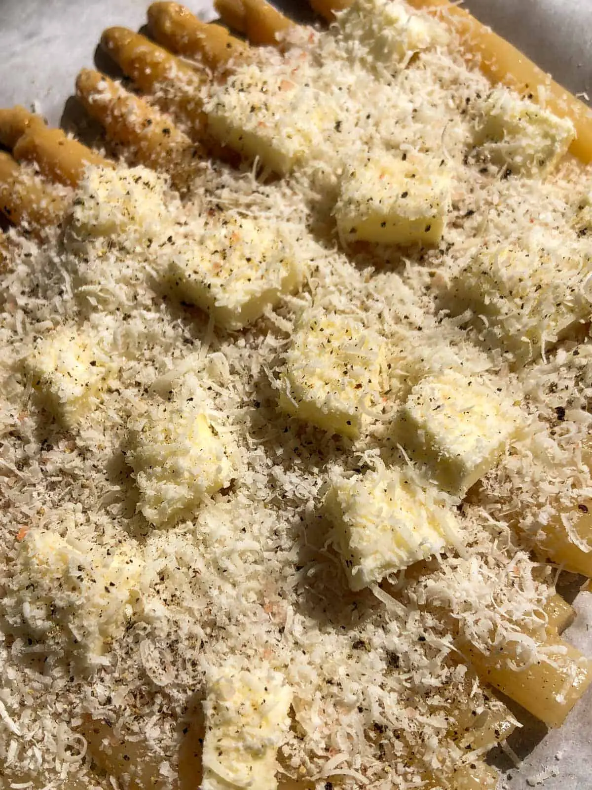 White asparagus spears topped with dots of butter, grated Parmesan cheese, and seasonings.
