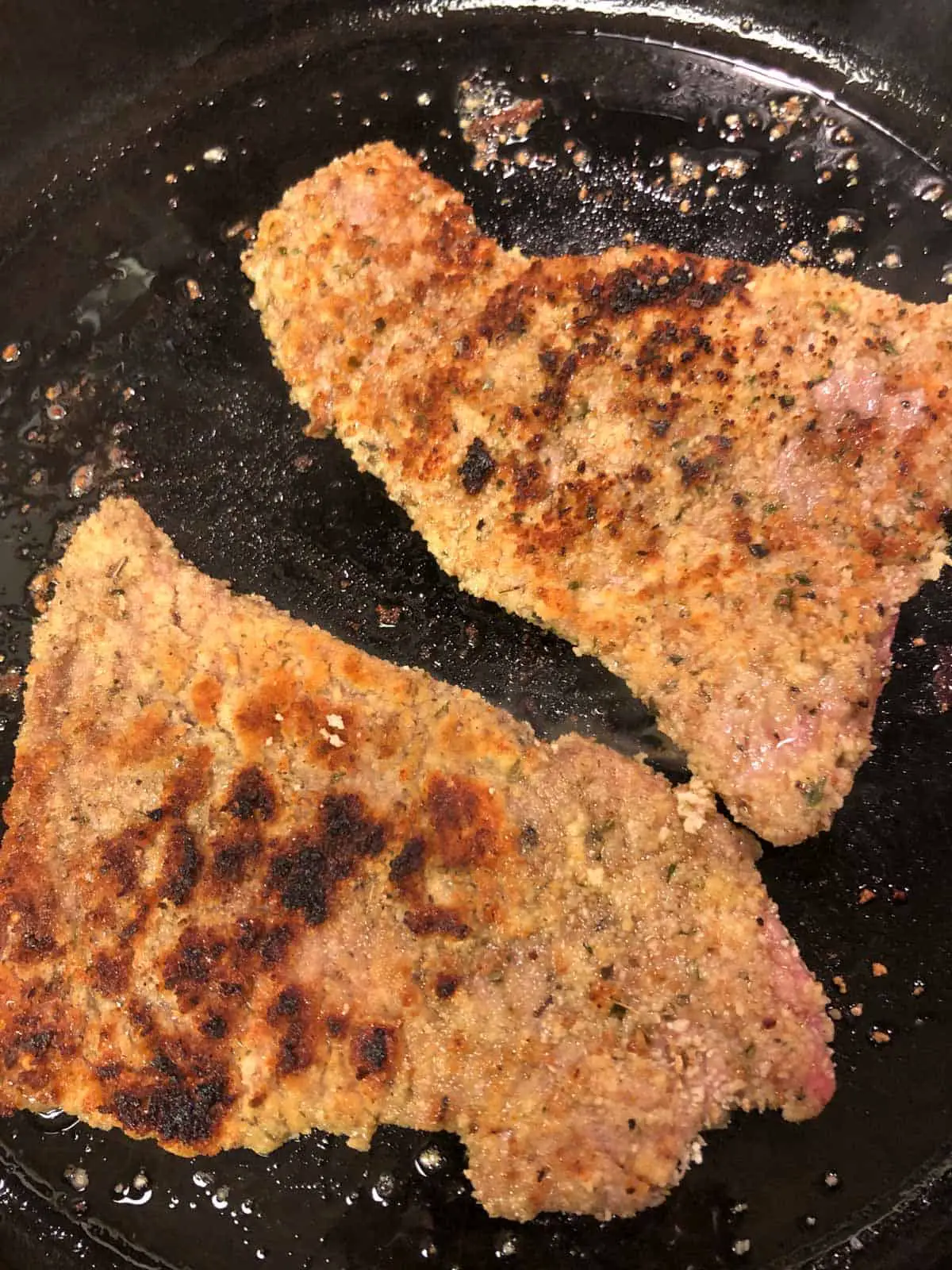 Two breaded veal cutlets that have been cooked in a cast iron pan.