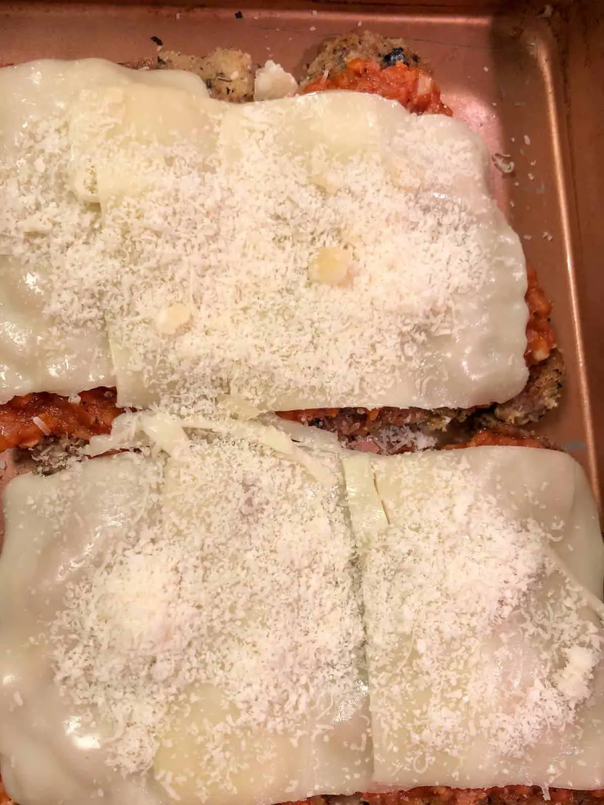 Breaded veal cutlets topped with tomato sauce then topped with slices of mozzarella cheese and freshly grated Parmesan cheese in a roasting pan.