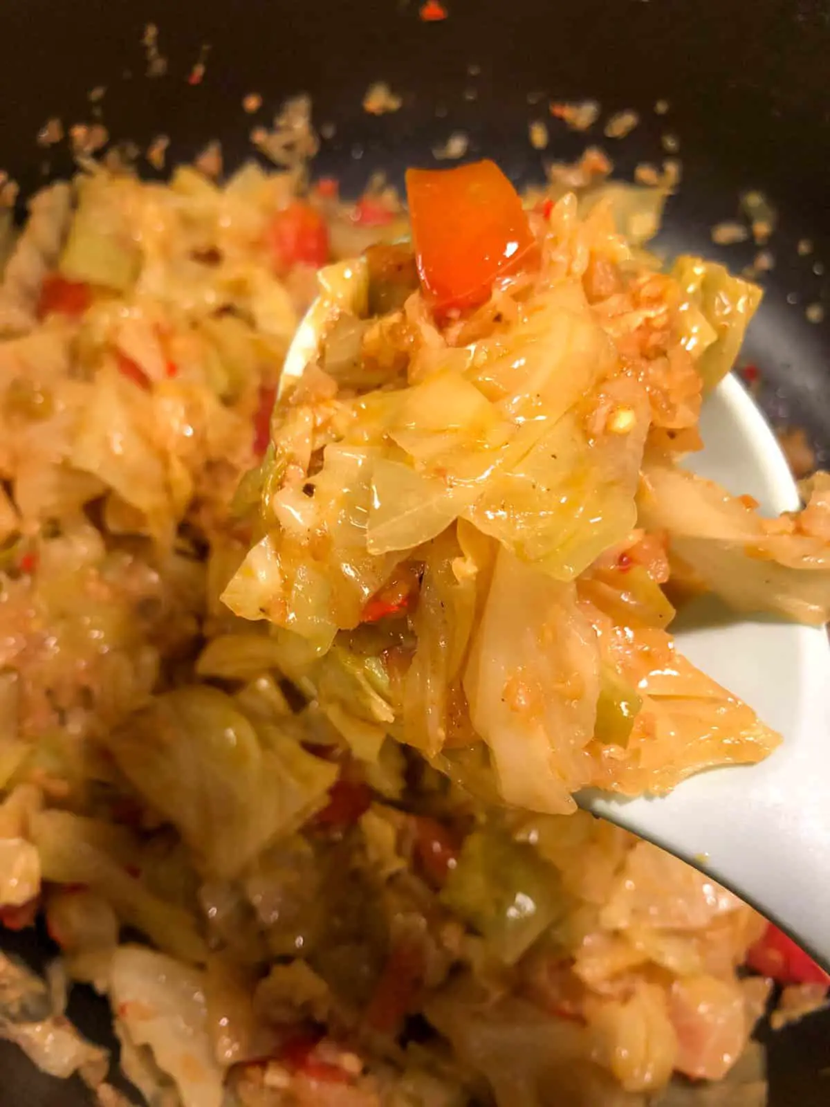Cooked Indian Spiced Cabbage with tomato in a large skillet with a spoonful of the cabbage in the foreground.